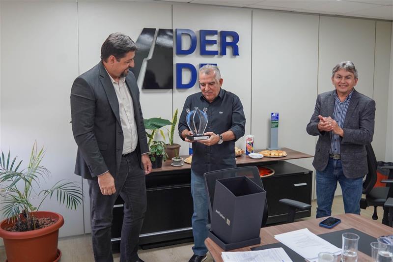Na segunda imagem temos a entrega do troféu da Softplan ao DER-DF com Fauzi Nacfur Júnior segurando a premiação ao lado de Adriano Marra e Jessé de Oliveira.